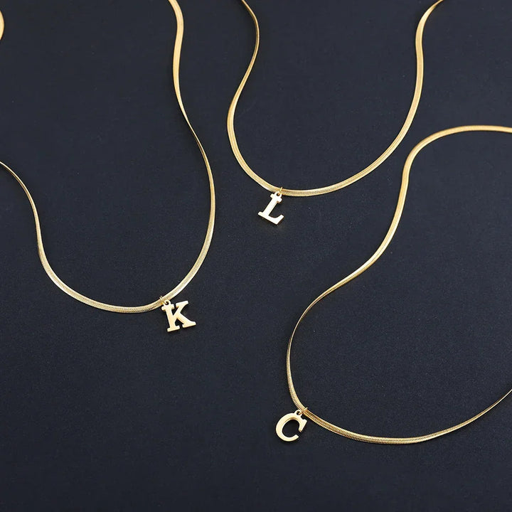 Gold initial necklaces with K, L, and C letter charms on black background, Rovelli jewelry