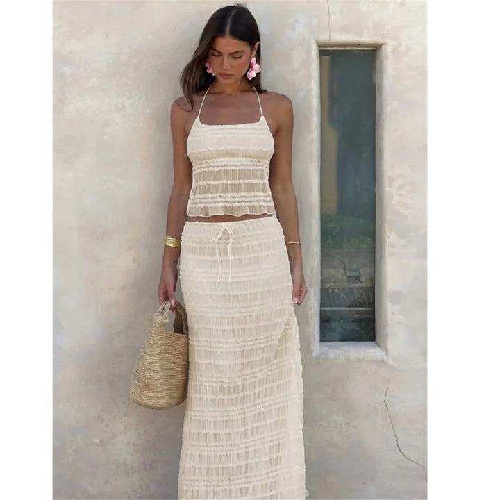 Woman in cream two-piece summer outfit holding straw bag, standing by textured wall, Rovelli