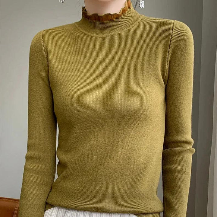 A person wearing a fitted, olive green ribbed sweater crafted from a cashmere blend with a high ruffled neckline and long sleeves, standing indoors against a neutral background.