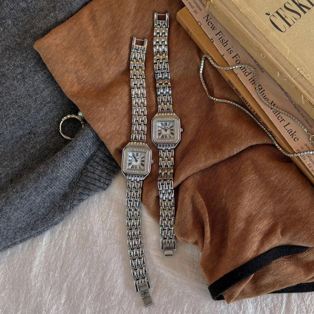 Rovelli silver square watches with chain bands on brown sweater and vintage books