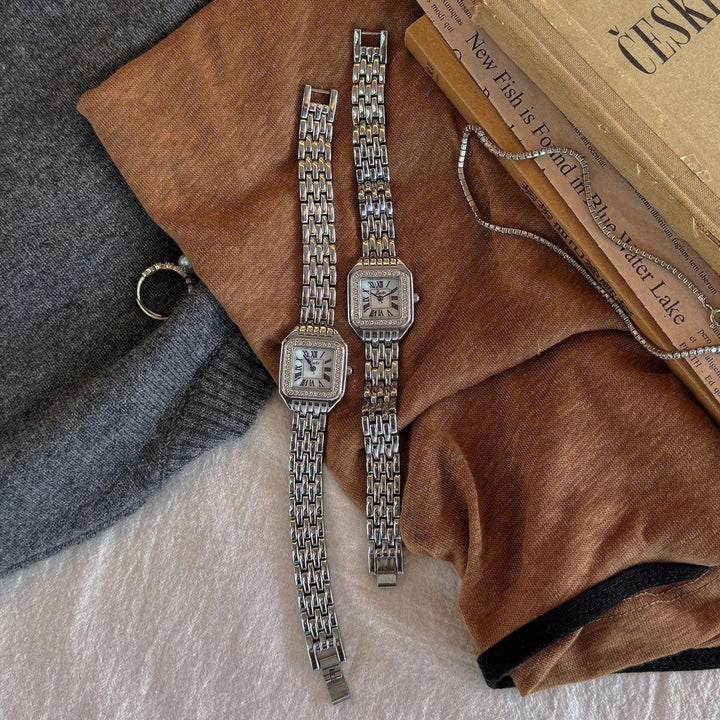Rovelli silver square watches with chain bands on brown sweater and vintage books