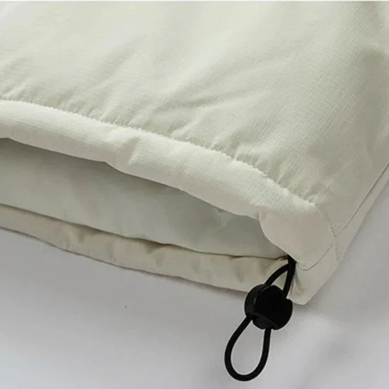 Close-up of a light beige windproof fabric jacket with an adjustable black drawstring and plastic toggle at the hem, showing the texture and stitching detail.