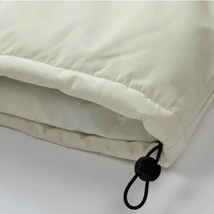 Close-up of a light beige windproof fabric jacket with an adjustable black drawstring and plastic toggle at the hem, showing the texture and stitching detail.