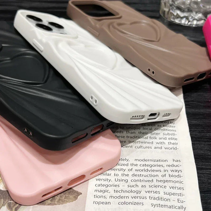 Several textured phone cases in black, white, pink, and brown with soft matte silicone finishes are stacked on top of an open book. The swirl-patterned cases offer full coverage protection and feature precise openings for the camera and charging ports.