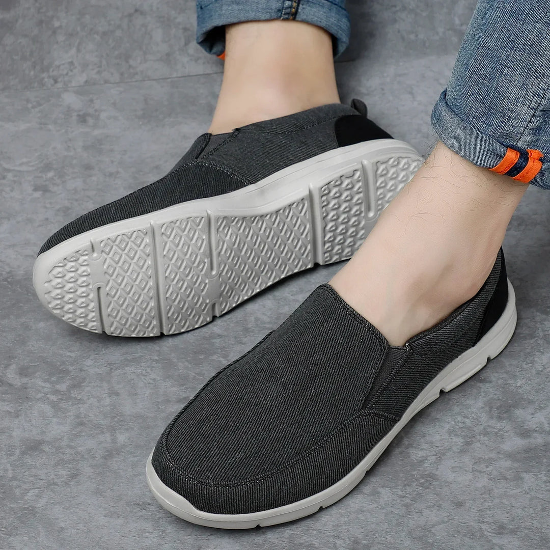 Rovelli black slip-on casual shoes with white soles on grey floor, worn with rolled jeans