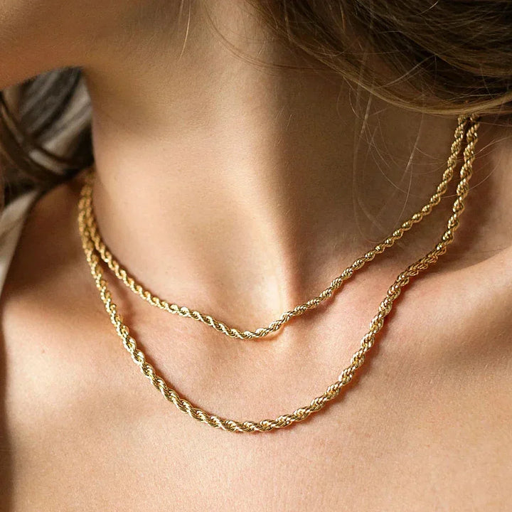 A close-up of a womans neck wearing two layered gold-toned jewelry rope chain necklaces with adjustable sizing, light brown hair partially visible on the left.