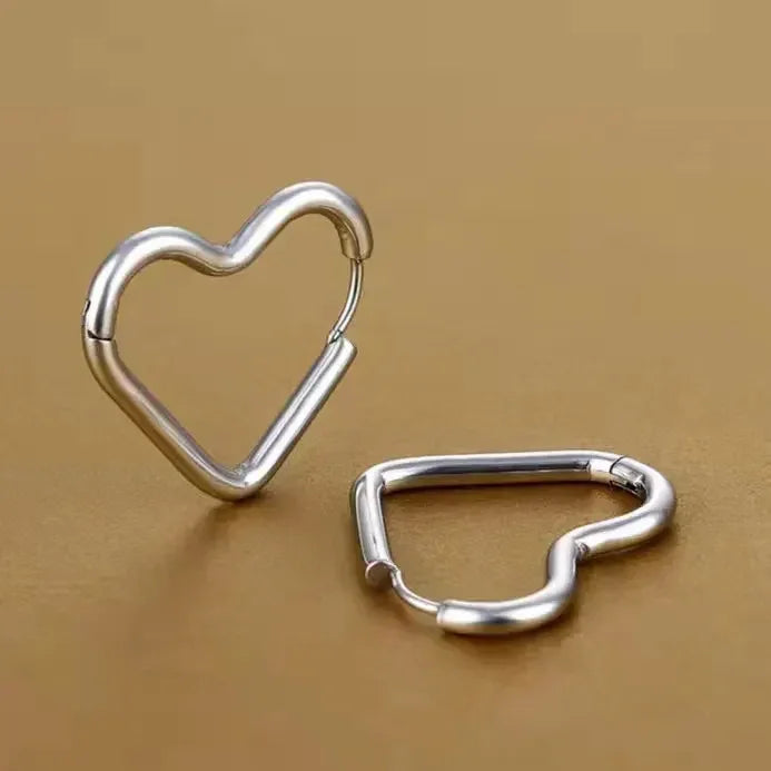 Two metallic heart-shaped Eternal Love Earrings rest on a smooth, gold-colored surface. One stands upright while the other lies flat, both highlighting their minimalist design and elegant craftsmanship.