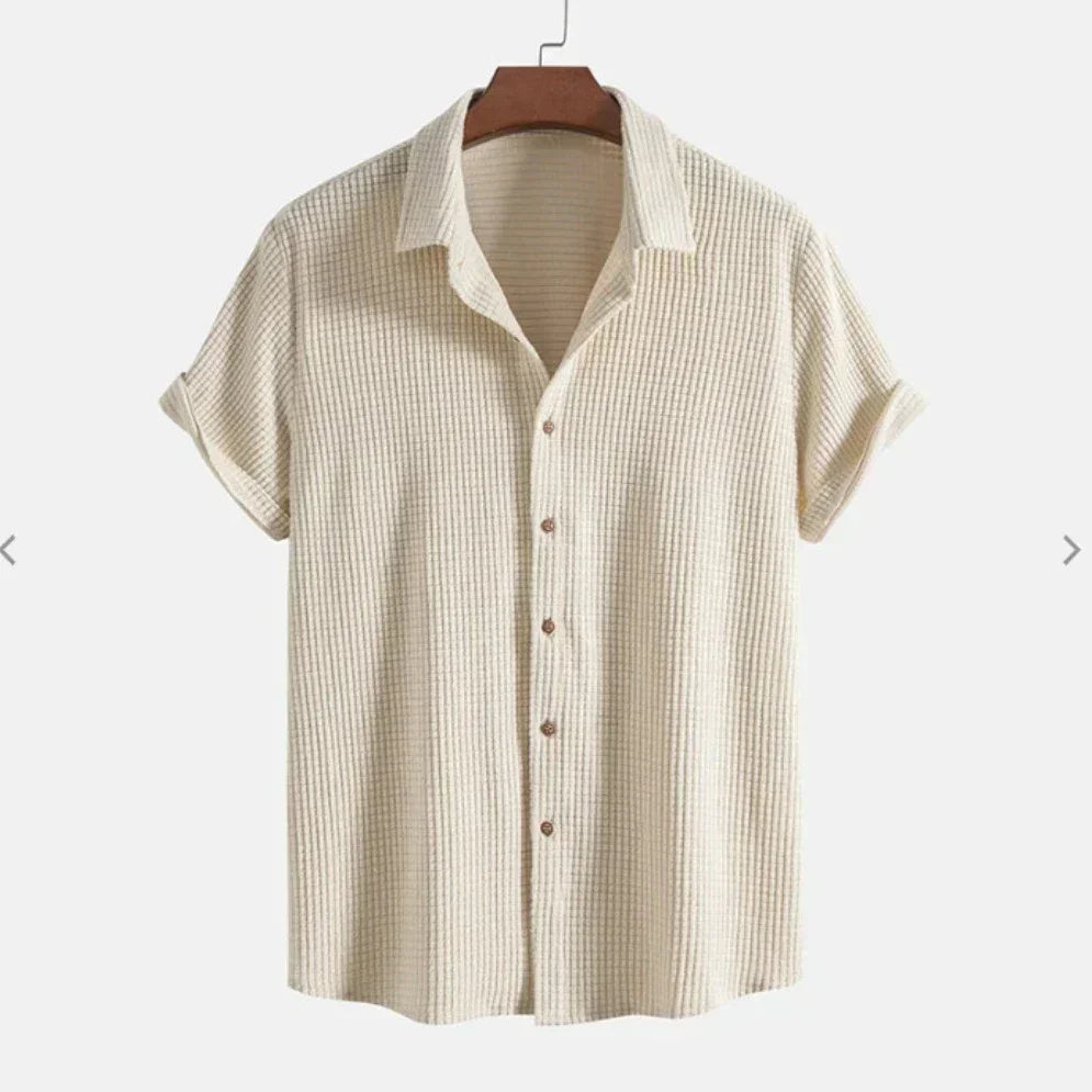 A short-sleeve, cream-colored Bayside Shirt featuring a textured button-up design and collar, crafted from a breathable cotton blend, displayed on a wooden hanger against a plain background.