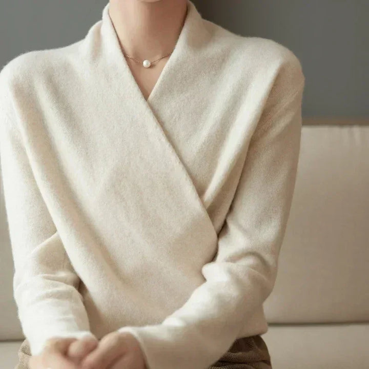Woman wearing cream knit wrap sweater and pearl necklace on beige sofa, Rovelli fashion