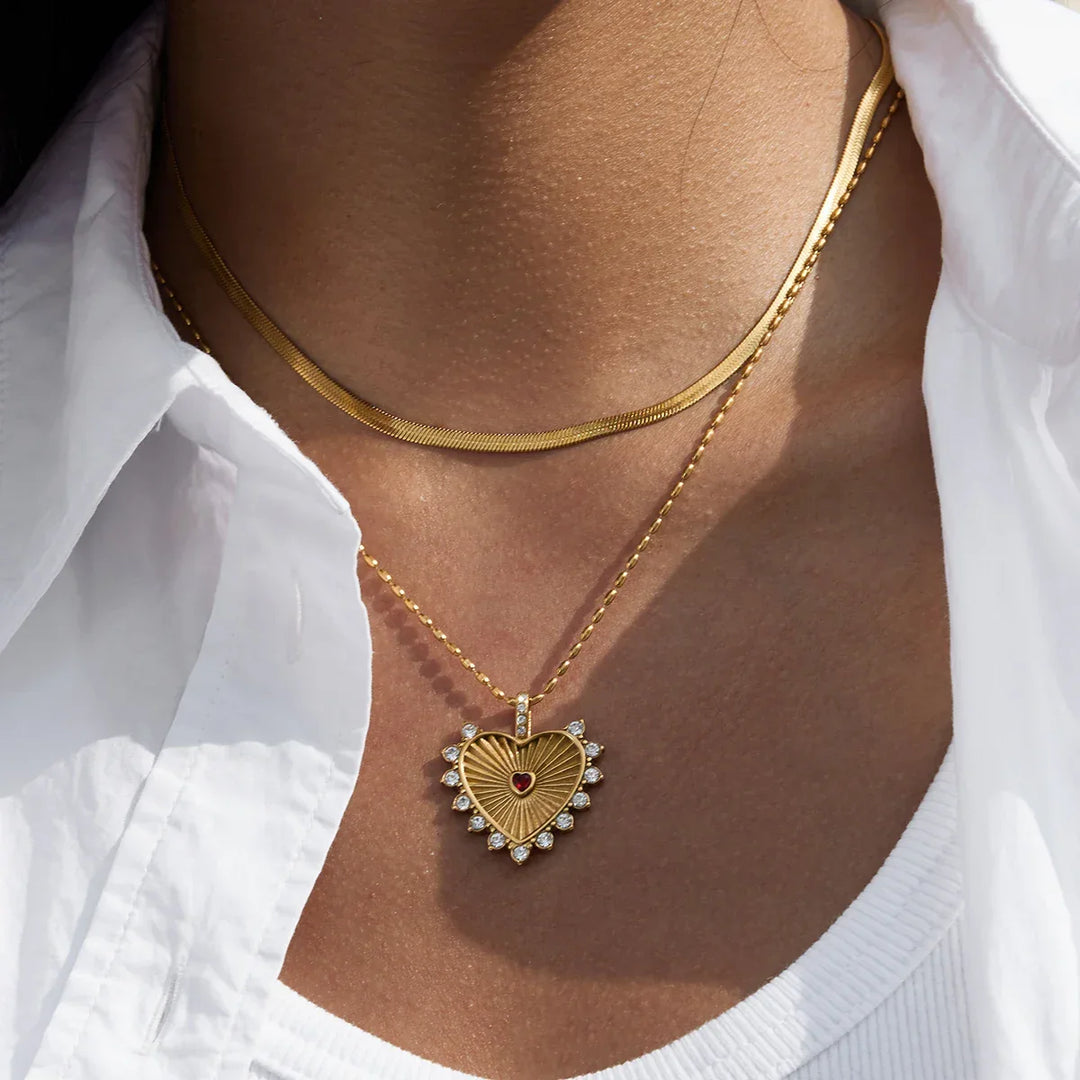Gold heart pendant necklace with diamanté accents from Rovelli, worn over white top