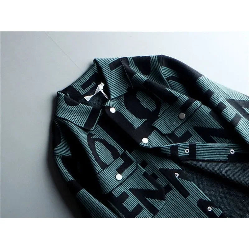 A close-up of a mens long sleeve coat with a bold, black and teal graphic pattern featuring large, overlapping letters. This Korean loose fit jacket is laid flat on a light gray surface.