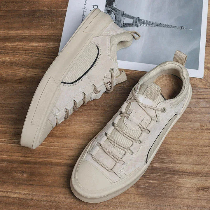 A pair of beige suede canvas shoes with thick soles and a unique lace design are placed on a wooden surface, partially covering a black and white photo of the Eiffel Tower.