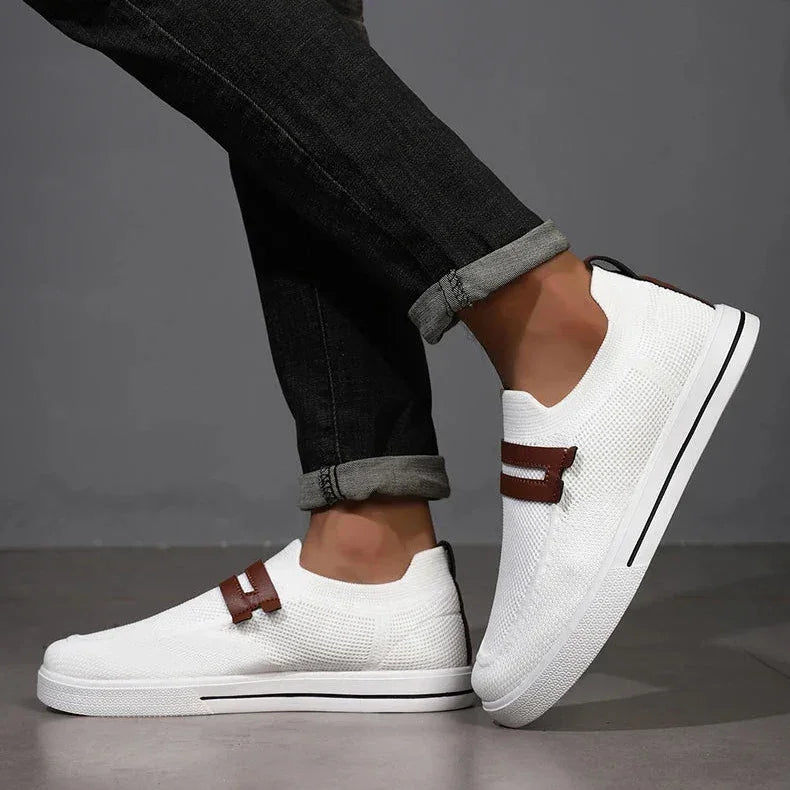Rovelli white slip-on sneakers with brown strap and black jeans on gray background