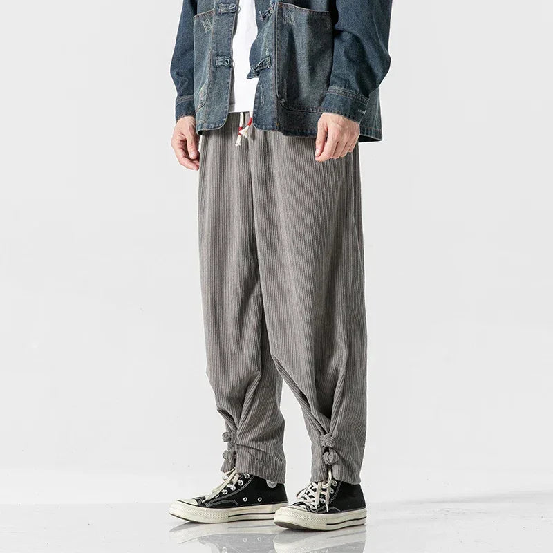 A person wears gray, loose-fitting cotton blend sweatpants with an adjustable fit and drawstring ties at the ankles, black Converse sneakers, a white shirt, and a denim jacket. Only the lower half of the body is visible.