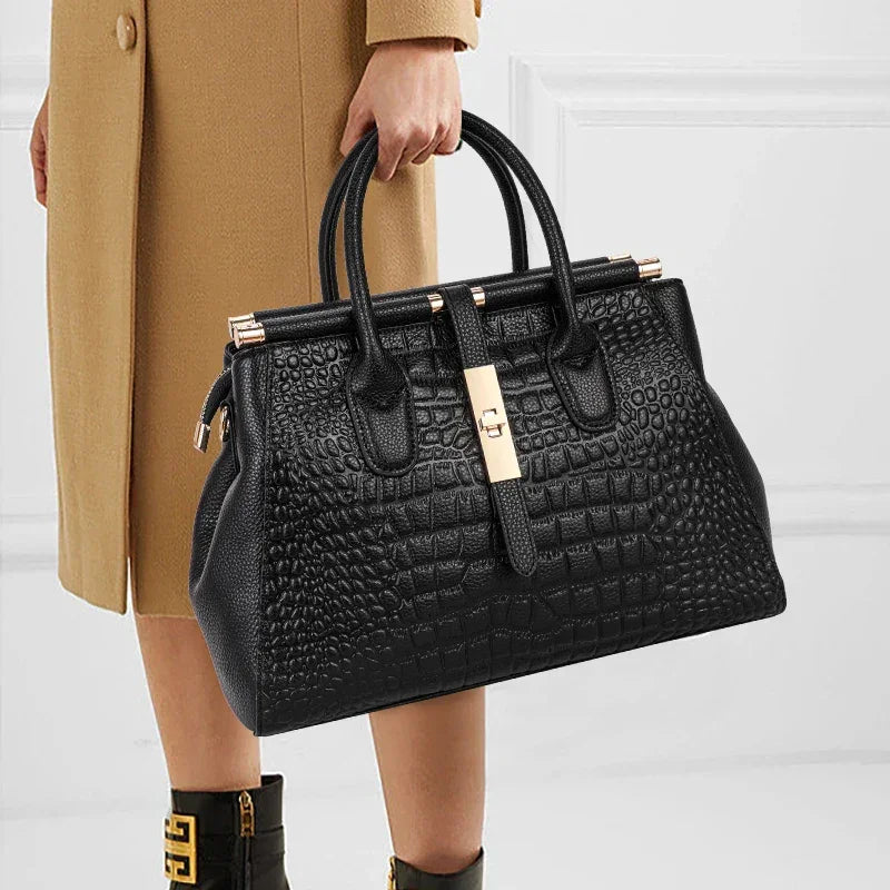Rovelli black crocodile-embossed handbag with gold clasp, held by a woman in a tan coat