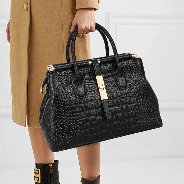 Rovelli black crocodile-embossed handbag with gold clasp, held by a woman in a tan coat