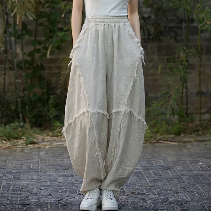 Loose beige linen pants with frayed seams, elastic waist, and pockets, outdoor setting, Rovelli