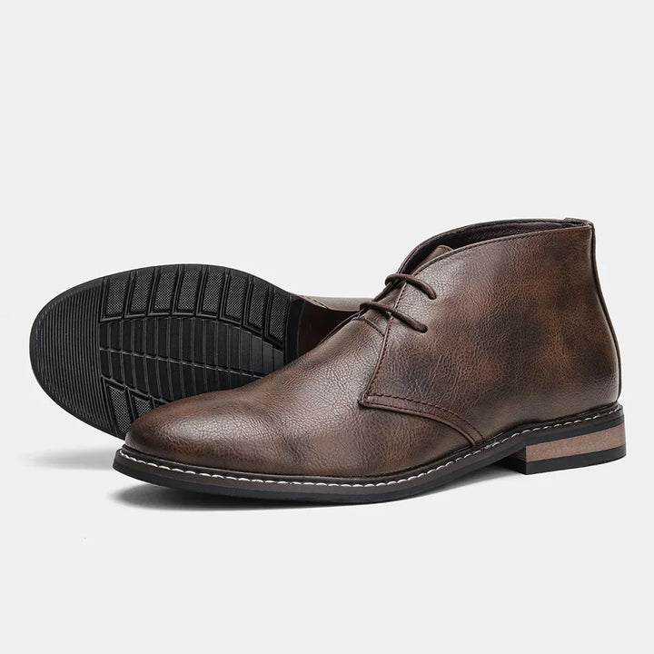 A pair of brown leather After-Ride Chukka boots with dark rubber soles, white stitching along the edge, and a low heel, displayed on a white background. One shoe stands upright while the other lies on its side.