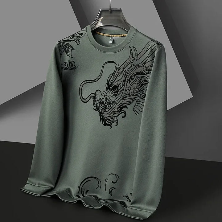 A green ultra-soft cotton crewneck with a large, detailed black dragon design on the front, displayed on a black hanger against a modern, geometric grey background.