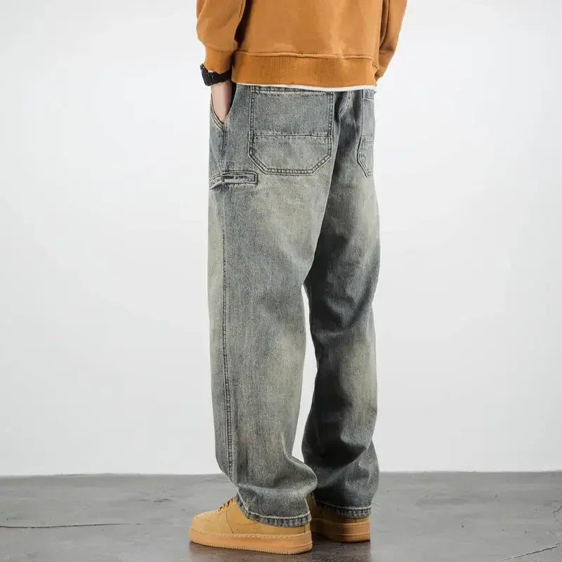 A person wearing a brown sweatshirt, classic fit stone washed jeans, and tan shoes stands with hands in pockets, facing away from the camera against a plain background.