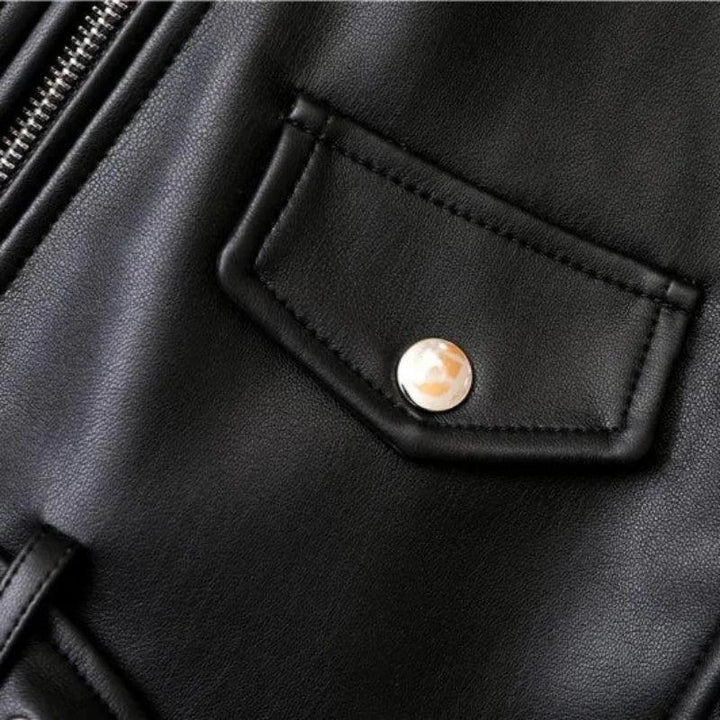 Close-up of a black leather jacket featuring a small flap pocket with a shiny metal snap button, part of a metal zipper on the left side, and detailing of an adjustable waist belt for a sleek, tailored fit.