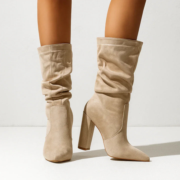 Beige suede slouchy heeled boots by Rovelli on model standing against white background