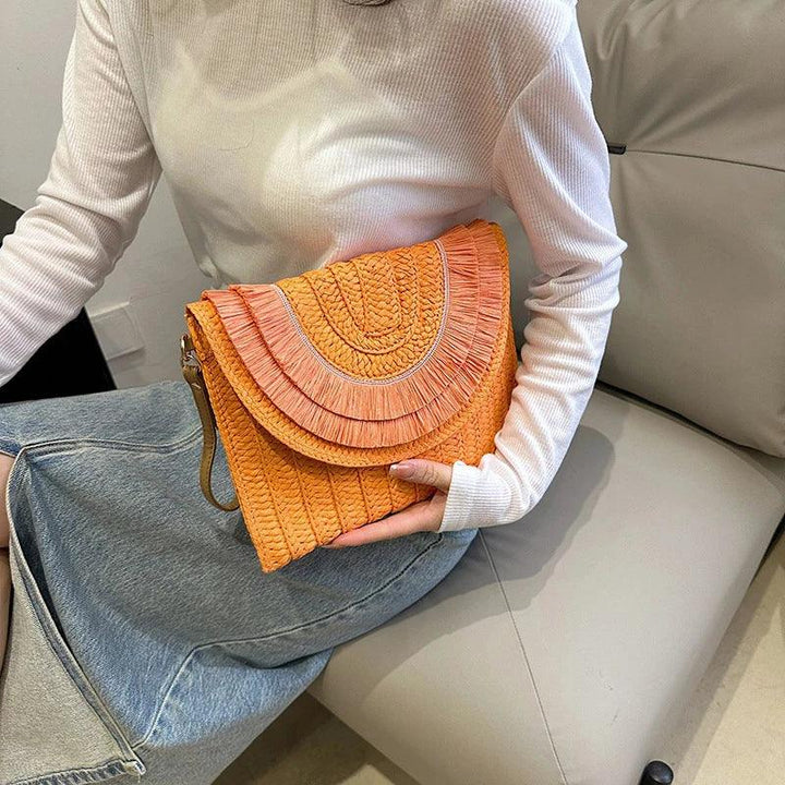 Woman holding an orange woven clutch bag on sofa, Rovelli accessories fashion