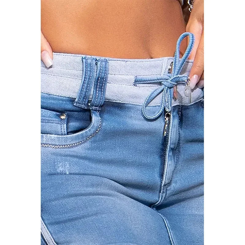 Close-up of a person wearing high waist light blue jeans crafted from premium cotton, featuring a unique waistband with a decorative bow and zipper details. The jeans have visible stitching, pockets, and the midriff and hand are partially visible.