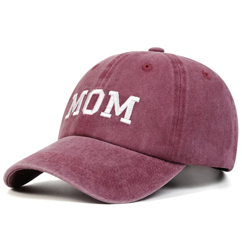 A pink vintage streetwear Mom & Dad cap with the word MOM embroidered in white capital letters on the front.