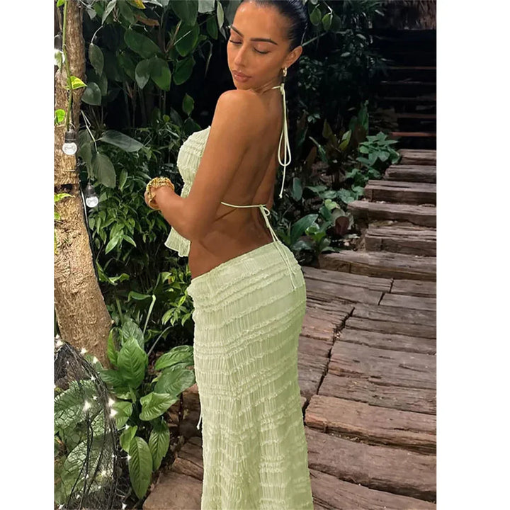 Woman in a light green backless dress standing on a wooden path with lush greenery, Rovelli fashion