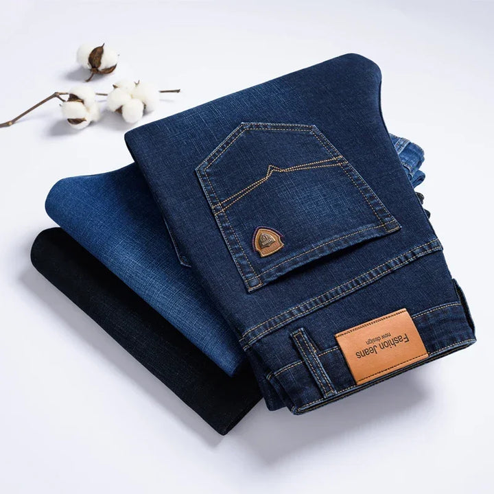 Stack of folded Rovelli dark and blue denim jeans with cotton branch on white background