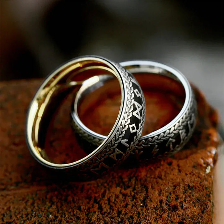 Two silver Viking Rune Rings with intricate engraved designs and gold interiors rest on a textured, reddish-brown brick surface. The couple's amulet rings feature patterns and symbols reminiscent of ancient or fantasy scripts.