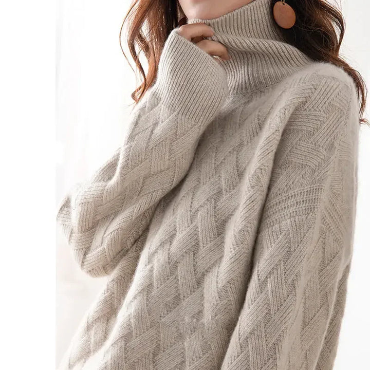 A person wearing an ultra soft, beige cable-knit turtleneck sweater with one sleeve partially covering their mouth; large round earrings are visible, and the background is softly lit.