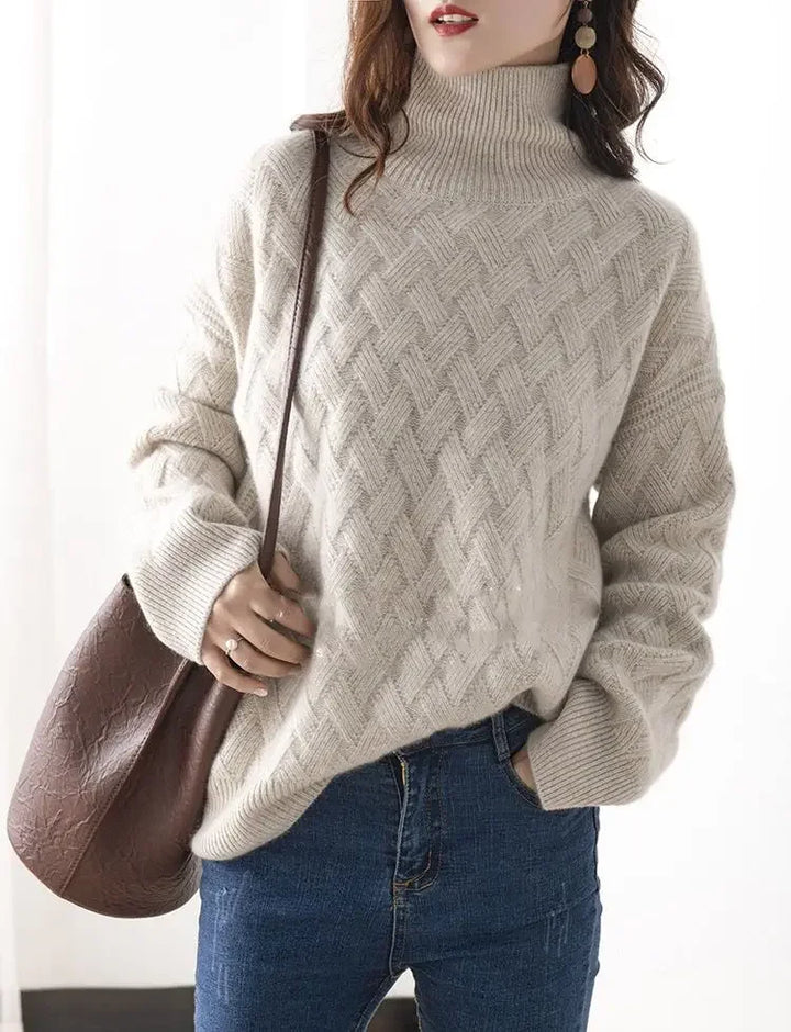 A woman wearing a cream-colored, ultra soft turtleneck sweater with a textured knit pattern and blue jeans, holding a brown shoulder bag. She has long, wavy hair and large dangling earrings. The background is softly lit.