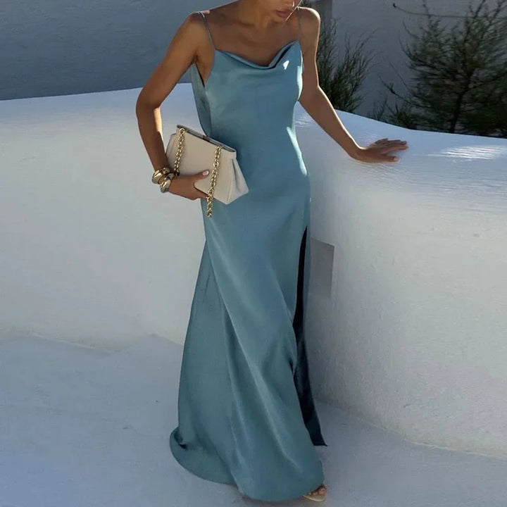 Woman in blue satin slip dress with side slit, holding beige clutch, Rovelli fashion