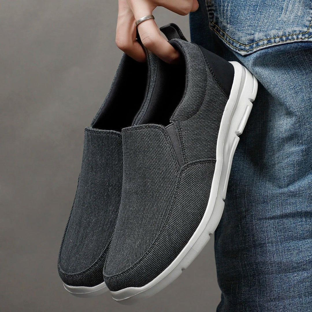 Rovelli dark gray slip-on casual shoes with white soles held beside blue jeans