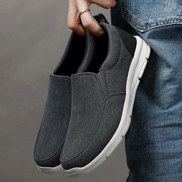 Rovelli dark gray slip-on casual shoes with white soles held beside blue jeans