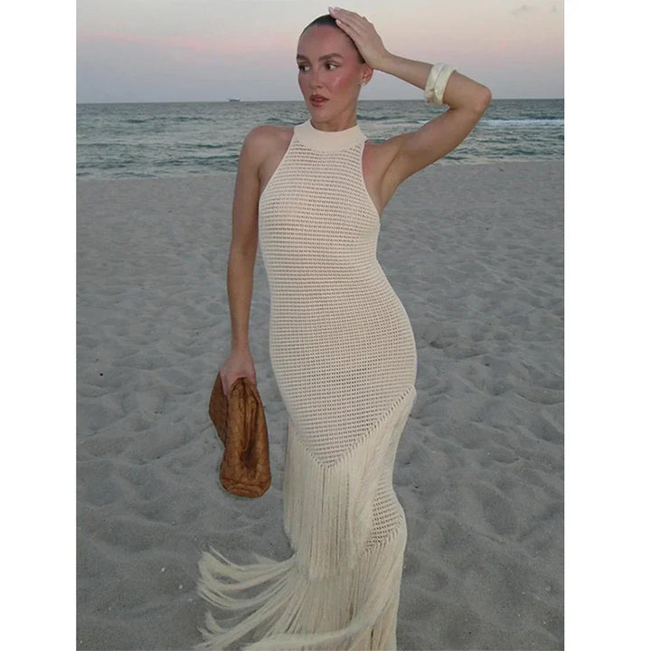 Woman on beach in cream crochet fringe dress holding brown clutch, Rovelli fashion