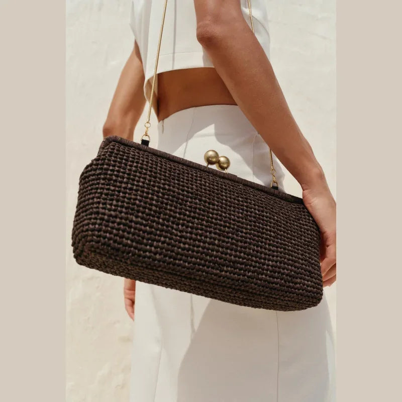 Woman in white outfit holding a large black woven shoulder bag with gold clasp, Rovelli fashion