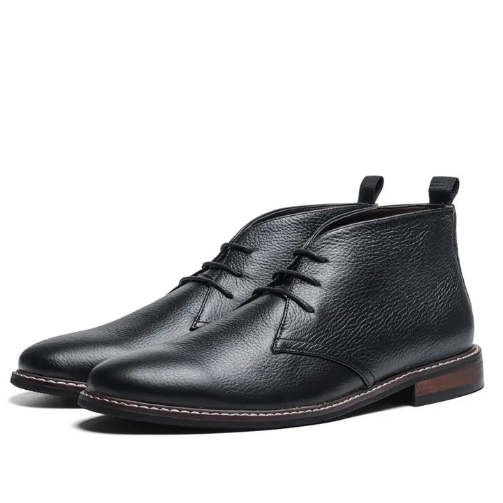 A pair of black leather After-Ride Chukka boots with a textured finish, brown outsoles, and low wooden heels, displayed on a white background.