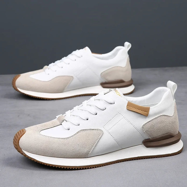 A pair of white and beige sneakers with brown accents and white laces, crafted from top-grain leather, displayed on a gray surface with a plain gray background.