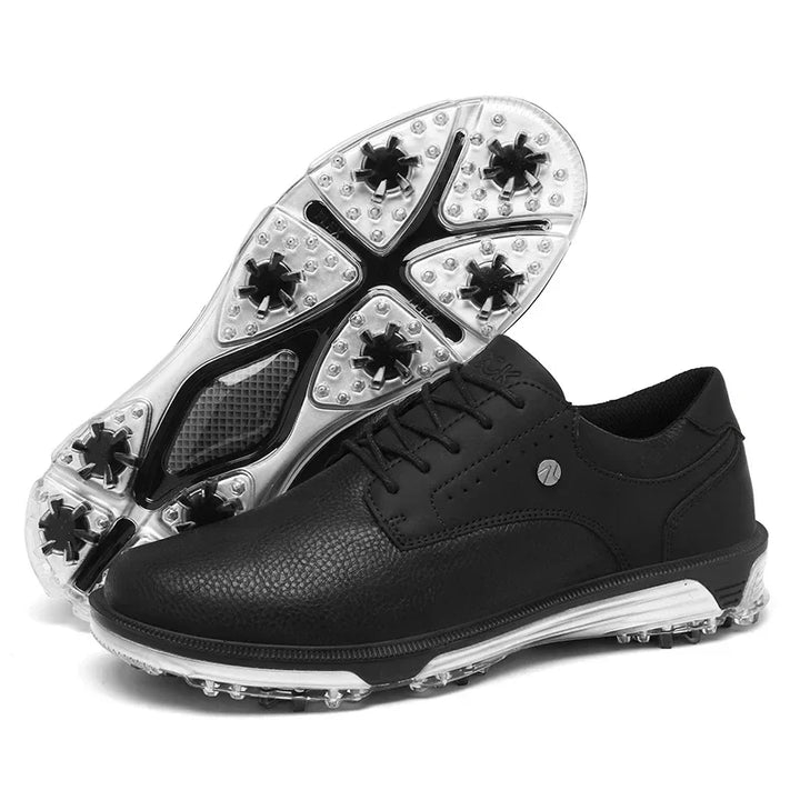 A pair of black golf shoes with textured leather uppers, a reinforced toe cap, and clear, spiked rubber soles—one shoe upright and the other positioned to display the sole’s tread and spikes.