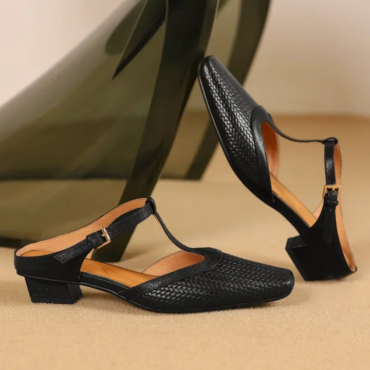 Rovelli black woven leather block heel sandals with T-strap and gold buckle on beige background