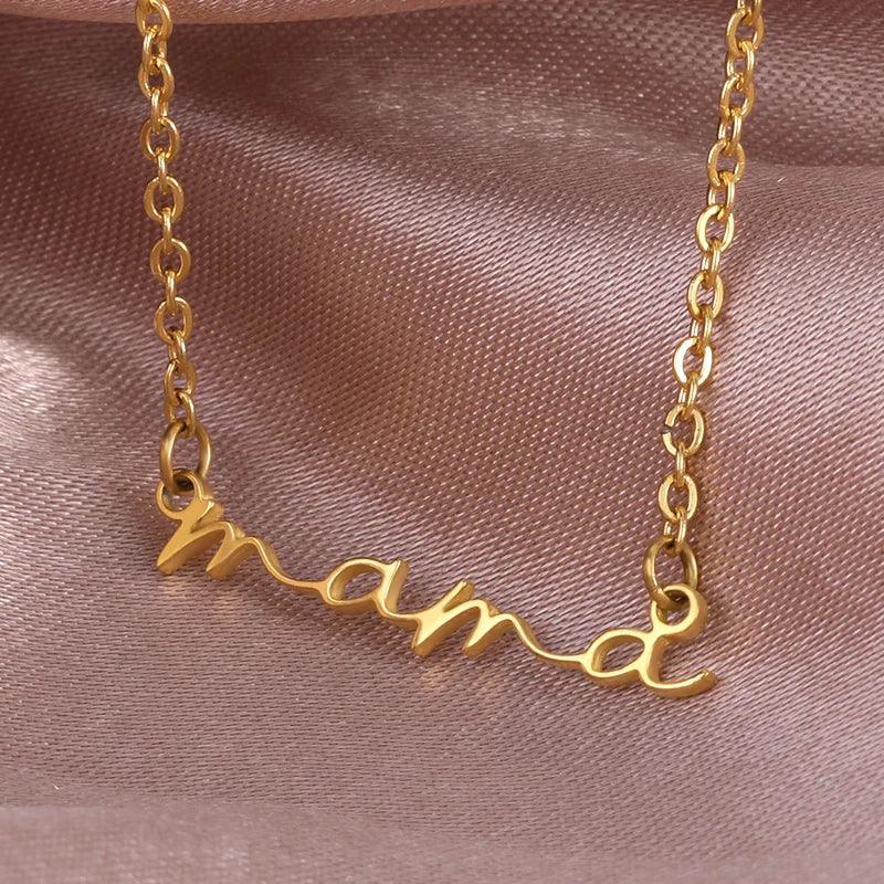 A gold-plated mama necklace with the word mama in cursive script, displayed on a soft, light pink satin fabric background—perfect as a thoughtful Mothers Day necklace.