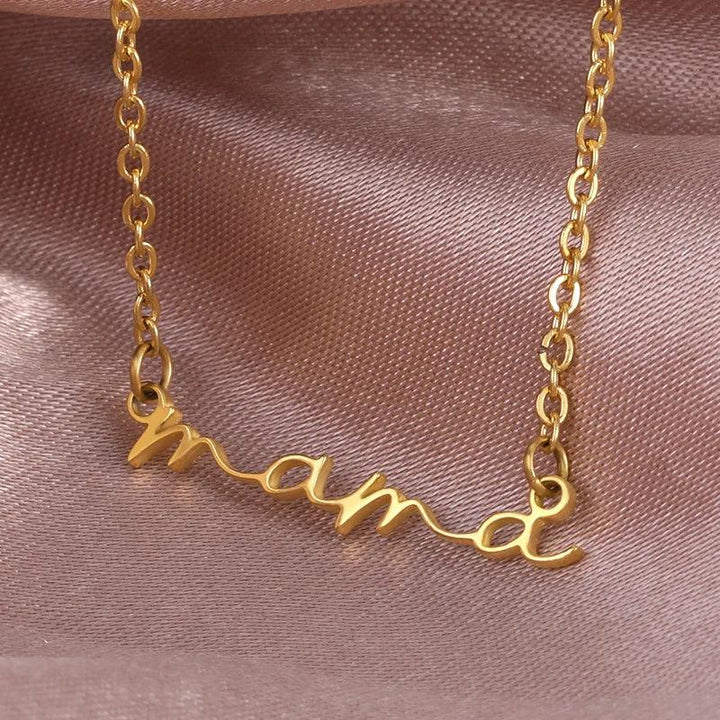 A gold-plated mama necklace with the word mama in cursive script, displayed on a soft, light pink satin fabric background—perfect as a thoughtful Mothers Day necklace.