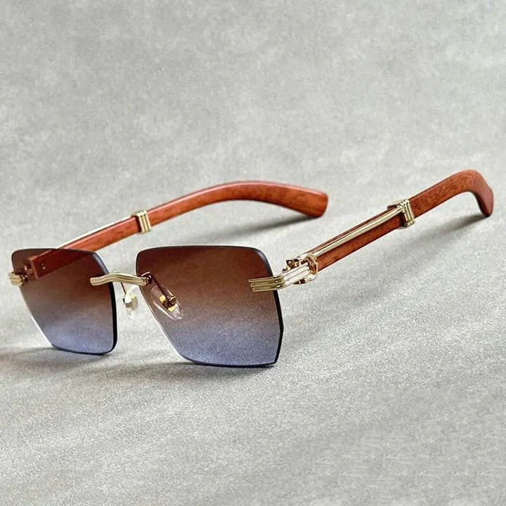 A pair of rimless sunglasses with gradient lenses, gold metal accents, and wooden temples, displayed on a light gray surface.