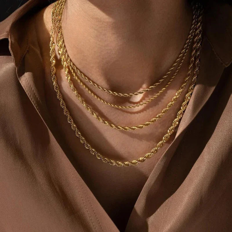 A person wearing a brown blouse with four layered gold rope chain necklaces crafted from non-fading materials around their neck, displayed against their skin and collar.