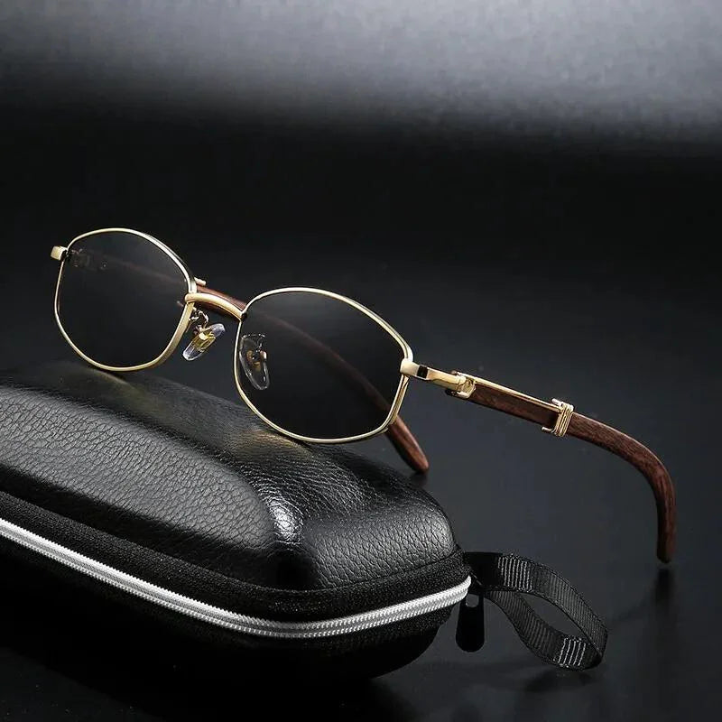 A pair of oval, gold-tone frames with brown arms rests on a closed black zippered glasses case against a dark background.