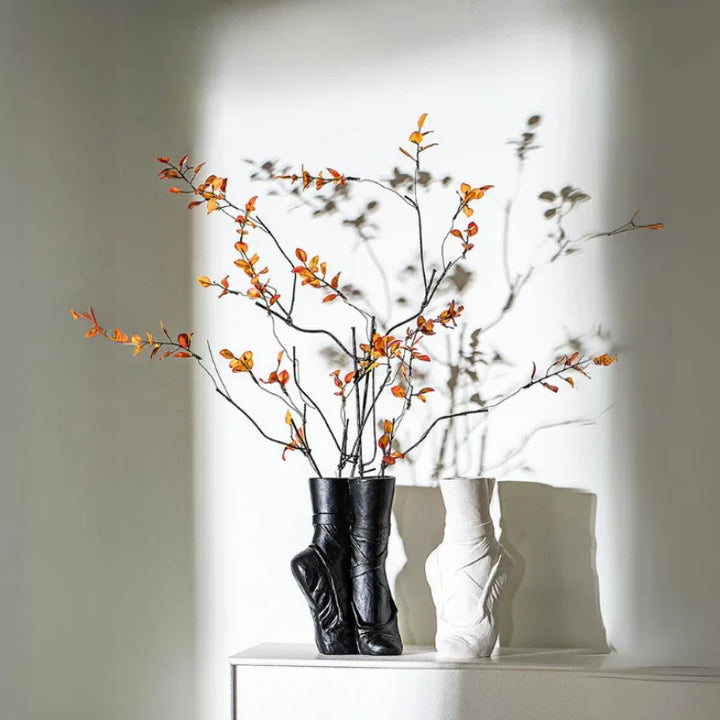 Two ballet-inspired ceramic vases, one black and one white, sit on a white surface. The black vase holds branches with small orange berries, casting dramatic shadows—perfect for contemporary chic décor.