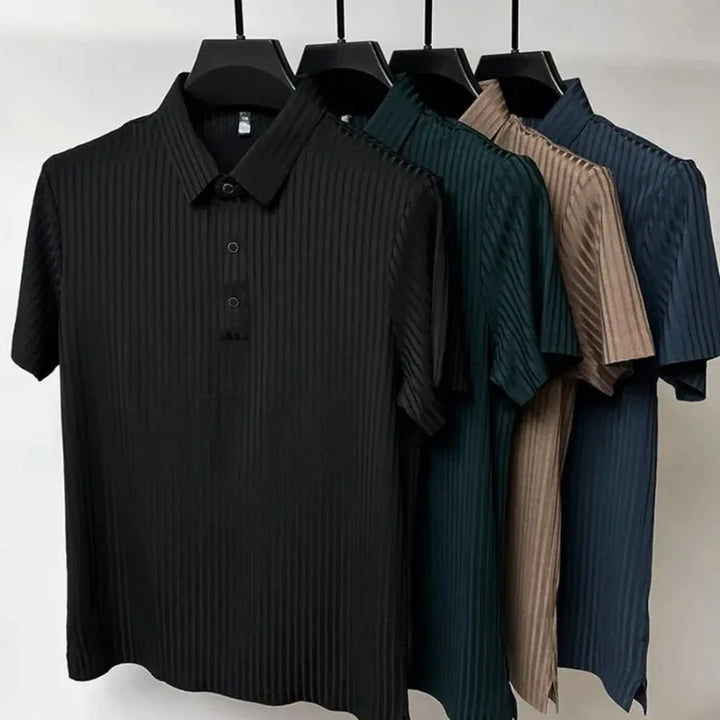 Four short-sleeved, collared shirts with vertical stripes and a classic polo design hang on black hangers. The shirts, in black, dark green, beige, and blue, are displayed against a plain white background.